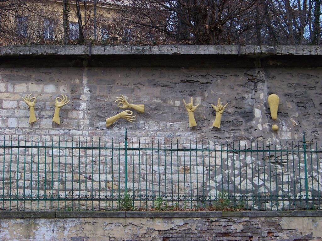 Sign language relief sculpture on a stone wall that means: "Life is beautiful, be happy and love each other", by Czech sculptor Zuzana Čížková on Holečkova Street in Prague-Smíchov
